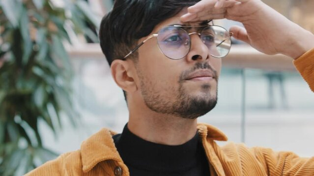 Close-up young indian guy waiting for date meeting puzzled man worries keeps hand on forehead looking out gesture peeking looks into distance with curious expression face waits for friend in search