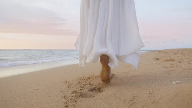 Cinematic summer vacation on beautiful tropical beach in slow motion on RED camera. Woman is elegant white waving dress walking barefoot by clear sandy golden beach. Sunset cloudy sky on background 6K