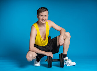 Obraz premium thin athlete in a yellow t-shirt and black shorts on a blue background. funny shakes muscles, goes in for sports, fitness
