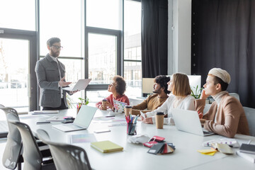 man with laptop talking to multiethnic advertising managers during meeting.