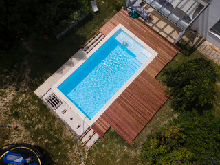 aerial drone flight over beautiful green garden with pool and the wooden deck of the pool is in...