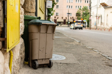Naklejka premium Green and beige trash bins on a sidewalk next to a building in an urban environment