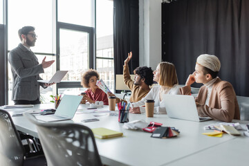 indian man with color samples raising hand during meeting with multiethnic team in ad agency.