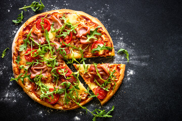 Traditional italian pizza with ham, cheese, tomatoes and arugula on black.