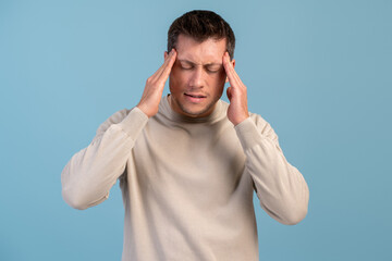 Fototapeta premium Young man wearing casual clothes standing over isolated blue background and suffering from headache desperate and stressed because pain and migraine. Hands on head