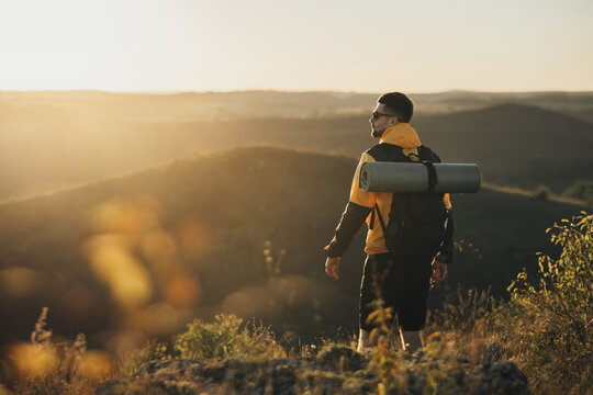 Back View of One Travel Man with Backpack with Camping Mat, Standing on the Top of Hill During Sunset, Male Nomad Enjoy His Solo Trip
