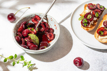 Toasts with soft cheese and baked with herbs sweet cherry berries on white concrete background. Roasted cherries. Delicious breakfast idea.