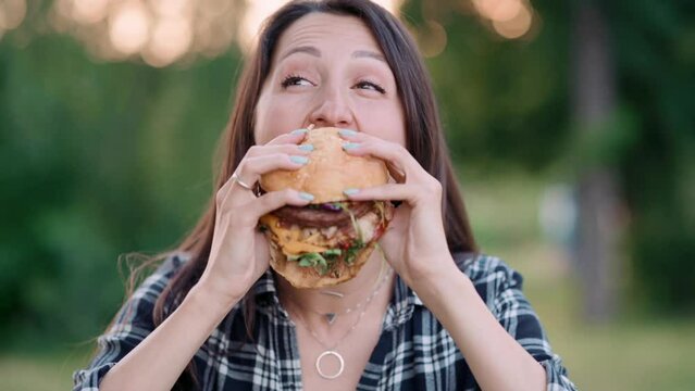 Young attractive hungry woman bites a big hamburger outdoor. Close up.