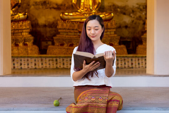 Asian buddhist woman is reading Sanskrit ancient Tripitaka book of Lord Buddha dhamma teaching while sitting in temple to chant and worship in the monastery