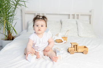 baby girl playing with wooden toy cubes on the bed at home in a bright room, the concept of early childhood development