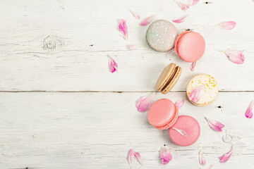 Macarons with peony flower petals on a white wooden background. Sweet dessert, pastel colors