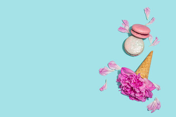 Ice cream waffle cones with peony and macarons on blue background. Sweet dessert, flower petals