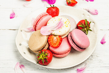 Macarons with strawberries and peonies flower petals, on a white wooden background
