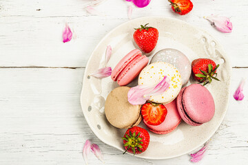 Macarons with strawberries and peonies flower petals, on a white wooden background