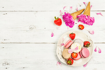 Naklejka na ściany i meble Macarons with strawberries and peonies flower petals, on a white wooden background