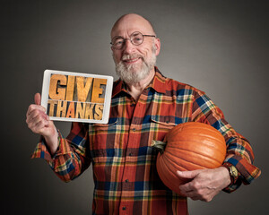 give thanks- a senior man with pumpkin is holding a digital tablet with sign in letterpress wood type, fall holidays greeting card