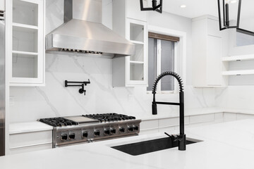 A luxury kitchen detail shot with a black faucet, white cabinets and marble countertops, and...