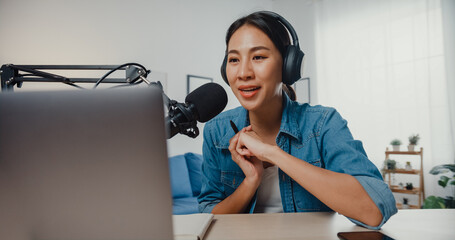 Happy asia girl record a podcast on laptop computer with headphones and microphone talk with...