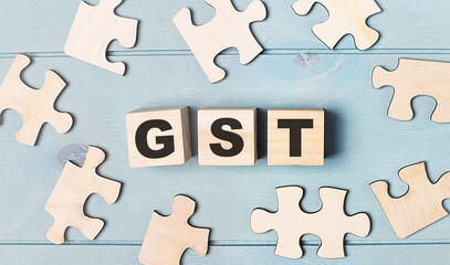Blank puzzles and wooden cubes with the text GST Goods and Services Tax lie on a light blue background.