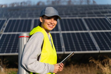 Fototapeta Photovoltaic power station. Professional woman engineer looking at the camera while using tablet computer for maintenance on ecological green field with solar panels. Female worker concept obraz