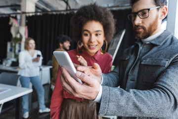 advertising manager in eyeglasses showing mobile phone to african american woman.