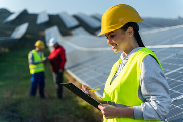 Caucasian female engineer in helmet looking at the documents and reading advice from the governance working on construction site of solar power plant