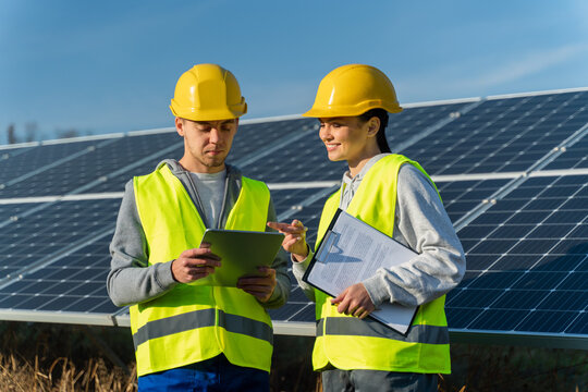 Waist up portrait view of male and female engineers in hardhat using tablet while working on maintenance of contemporary photovoltaic panels on solar power station