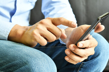 Obraz na płótnie Canvas Hombre latino sosteniendo su telefono movil mientras escribe. Vista lateral.