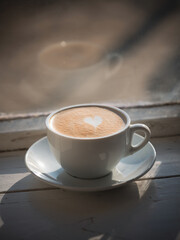 Cup of cappuccino with latte art in the shape of a heart by the window