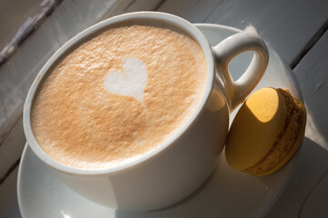 Cup of cappuccino with macaron under sunlight on the windowsill