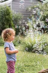 Curly haired toddler girl playing in the backyard with bubbles on a summer day