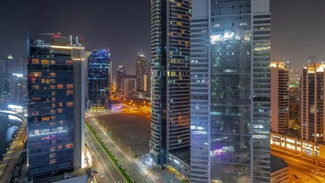 Cityscape of skyscrapers in Dubai Business Bay and downtown with water canal aerial during all night timelapse. Modern skyline with illuminated towers and waterfront. Lights turning off