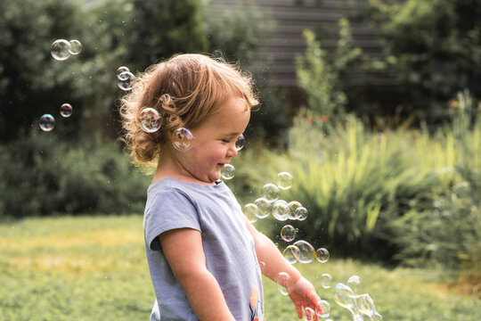 Toddler girl playing with bubbles in backyard on summer day