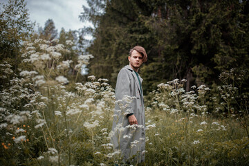 Fototapeta premium man in a gray coat in the summer in the forest grass and trees. The concept of the philosopher's walk in nature, nostalgia and memories.