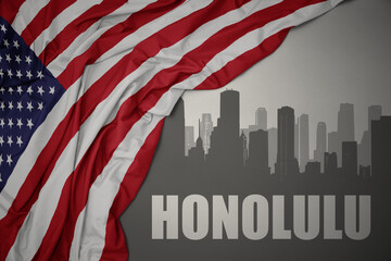 abstract silhouette of the city with text Honolulu near waving colorful national flag of united states of america on a gray background.