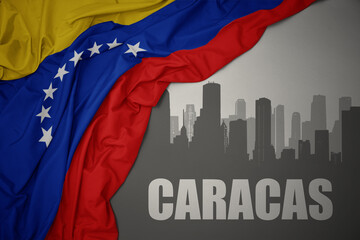 abstract silhouette of the city with text Caracas near waving colorful national flag of venezuela on a gray background.