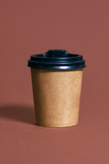 Disposable coffee cup for a cafe on a brown vertical background. Brown cardboard eco coffee cup mockup. Disposable plastic and paper template for hot drinks