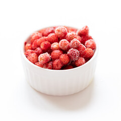 Frozen red wild forest strawberry in white bowl on white. Selective focus. Square photo.