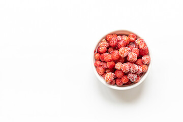 Frozen red wild forest strawberry in white bowl on white background. Copy space. Top view.