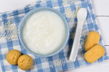 Rice porridge for the baby from ground cereals in a blue bowl, a spoon, cookies on a blue cloth napkin. Baby nutrition.