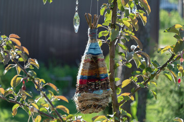 a knitted bird feeder for birds and squirrels hangs on a tree branch in a sunny garden