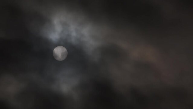 Eerie dark and stormy sky with bright orb, sun or moon, shining bright as thick clouds pass.
