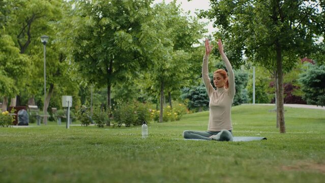 Woman practices yoga and relaxing in nature outdoors. Caucasian female doing yoga sitting on yoga mat. Meditation in nature.