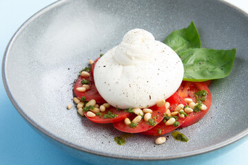 Buratta cheese and tomatoes in a bowl. Decorated with pine nuts.