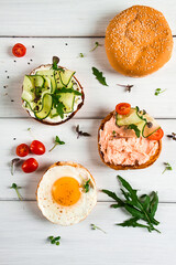 Assortment of sandwiches, white bread, fried egg, cream cheese and cucumber, capelin caviar, sesame bun, breakfast, on a white table, vertical, no people,