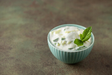 Indian Fresh sauce called Raita with herbs, dahi and sliced cucumber in a bowl on the table.