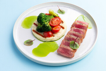 Fried tuna and vegetables in a plate on a blue background.