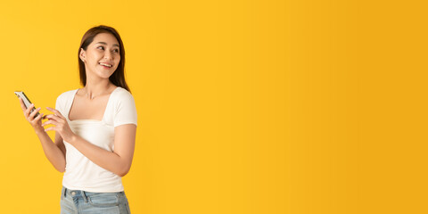 Surprise happy asian beautiful woman isolate on yellow background using smartphone look at blank copy space area