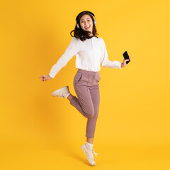 Fototapeta na wymiar Cute young asian teenage woman using smartphone wearing headphone isolated on yellow background jumping and dancing