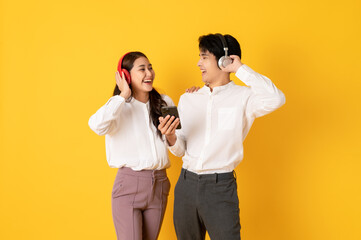 Two Young good looking asian couple using smartphone and headphone listen to music isolated on yellow background